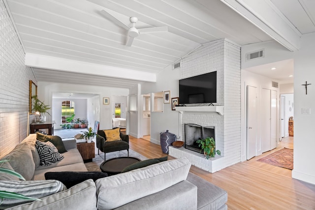 living room featuring lofted ceiling with beams, a brick fireplace, hardwood / wood-style floors, ceiling fan, and brick wall