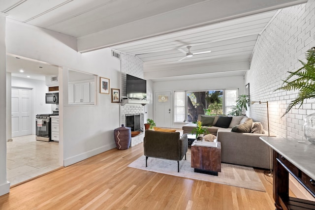 living room featuring light hardwood / wood-style flooring, brick wall, a fireplace, and ceiling fan