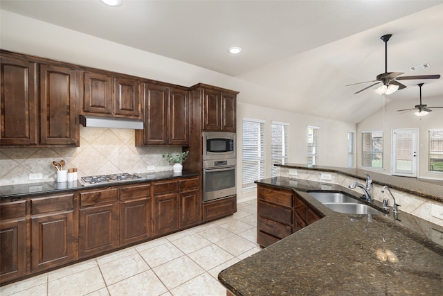 kitchen with appliances with stainless steel finishes, dark stone counters, vaulted ceiling, dark brown cabinetry, and sink