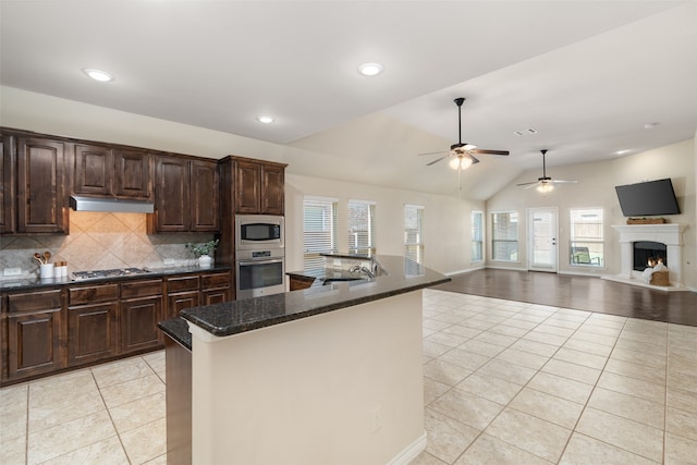 kitchen with appliances with stainless steel finishes, light tile patterned flooring, an island with sink, dark stone counters, and lofted ceiling