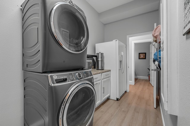 laundry room with stacked washer / drying machine, cabinets, and light hardwood / wood-style floors