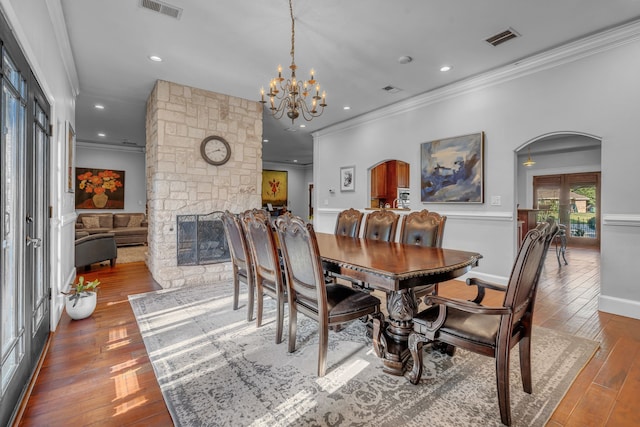 dining room featuring crown molding, a notable chandelier, dark hardwood / wood-style flooring, and a stone fireplace