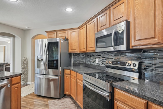 812 Redbud Rd, Burleson, TX 76028 - kitchen with appliances with stainless steel finishes, decorative backsplash, light wood-style flooring, a textured ceiling, and arched walkways