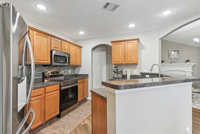 kitchen featuring light hardwood / wood-style floors, tasteful backsplash, appliances with stainless steel finishes, and a textured ceiling