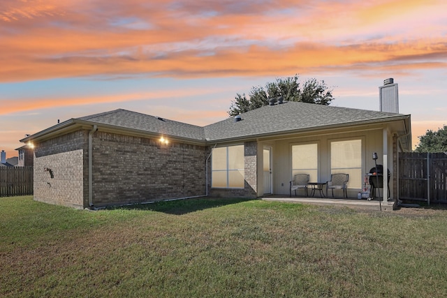 back house at dusk featuring a patio and a lawn