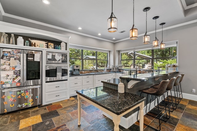 kitchen with stainless steel appliances, dark stone counters, decorative light fixtures, white cabinets, and a breakfast bar area