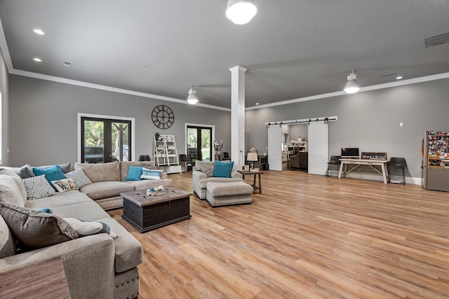 living room with french doors, crown molding, light wood-type flooring, and a barn door