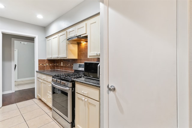 kitchen with tasteful backsplash, cream cabinets, light tile patterned flooring, stainless steel gas range oven, and dark stone countertops