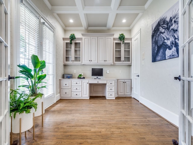 home office with beam ceiling, built in desk, light hardwood / wood-style flooring, crown molding, and coffered ceiling