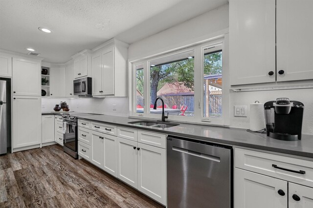 kitchen with appliances with stainless steel finishes, a textured ceiling, white cabinetry, dark hardwood / wood-style floors, and sink