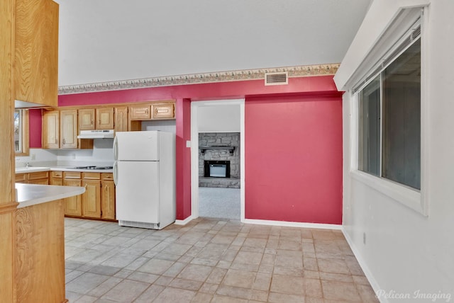 kitchen with stovetop, sink, a stone fireplace, and white fridge