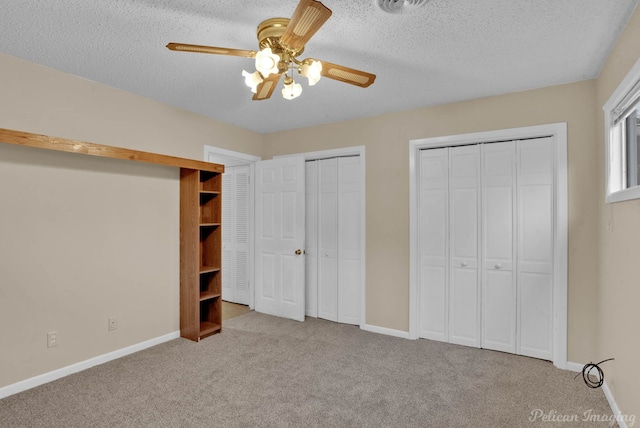 unfurnished bedroom featuring light carpet, multiple closets, a textured ceiling, and ceiling fan