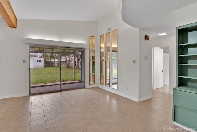 tiled empty room featuring built in shelves, vaulted ceiling, and a textured ceiling