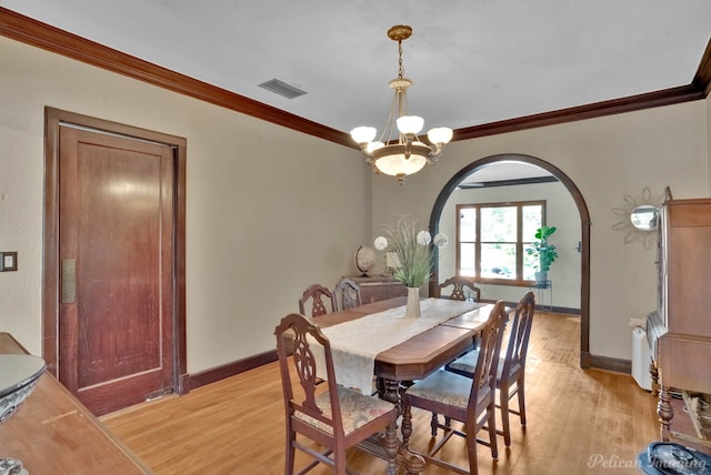 dining area with arched walkways, a notable chandelier, visible vents, light wood finished floors, and crown molding