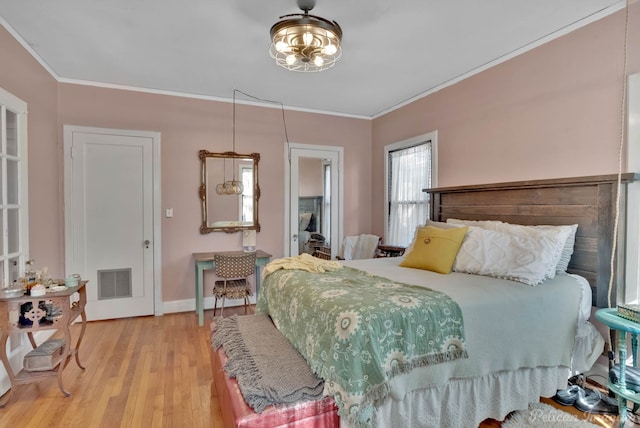 bedroom featuring baseboards, light wood-type flooring, visible vents, and crown molding