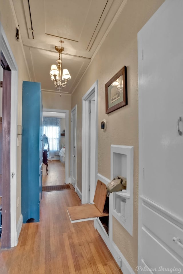 hallway featuring a chandelier, ornamental molding, light wood-style flooring, and baseboards