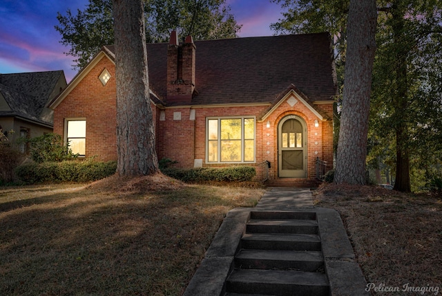 view of front facade with a yard, roof with shingles, and brick siding