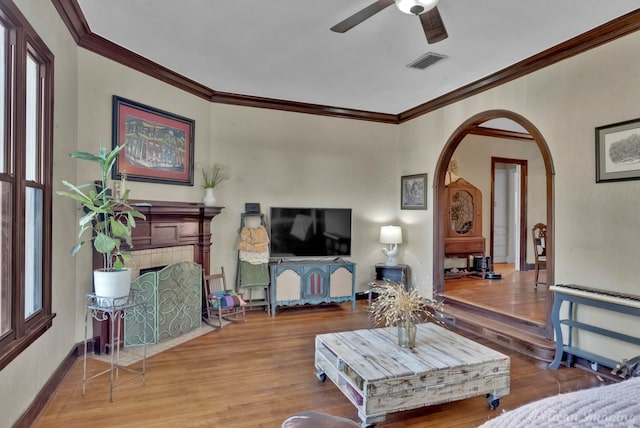 living room with visible vents, arched walkways, a tiled fireplace, and wood finished floors