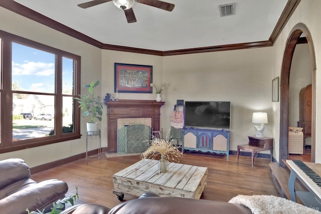 living room featuring a tiled fireplace, wood-type flooring, and ornamental molding