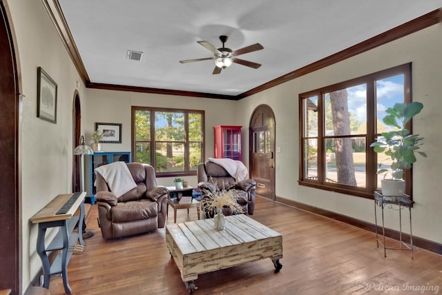 living room featuring arched walkways, visible vents, ornamental molding, light wood-type flooring, and baseboards