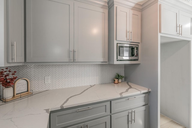 kitchen with tasteful backsplash, gray cabinetry, stainless steel microwave, and light stone counters