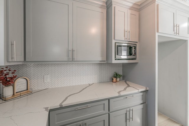 kitchen with decorative backsplash, light stone countertops, stainless steel microwave, and gray cabinetry