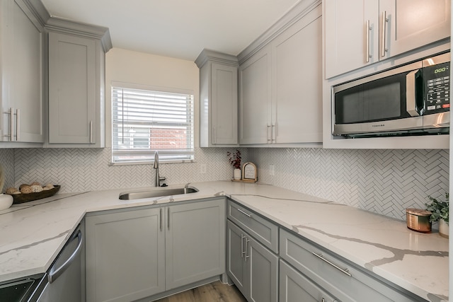 kitchen featuring sink, light hardwood / wood-style flooring, decorative backsplash, light stone counters, and stainless steel appliances