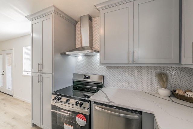 kitchen featuring decorative backsplash, light stone counters, wall chimney range hood, and appliances with stainless steel finishes