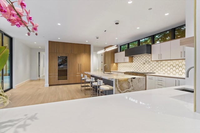 kitchen featuring premium range hood, white cabinetry, hanging light fixtures, and sink