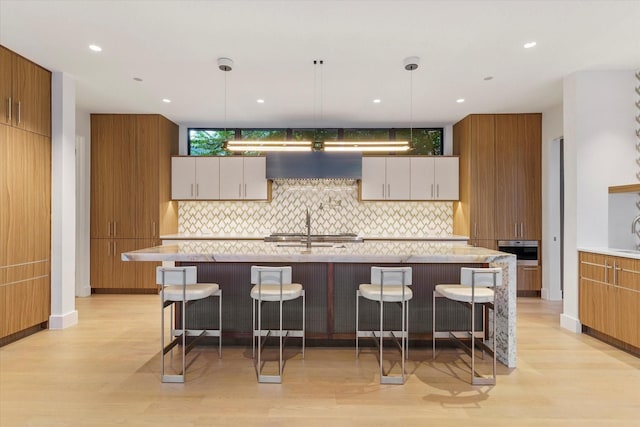 kitchen featuring white cabinets, decorative light fixtures, custom range hood, and an island with sink