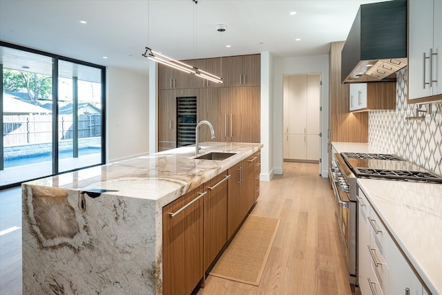 kitchen with white cabinetry, sink, wall chimney exhaust hood, decorative light fixtures, and high end range