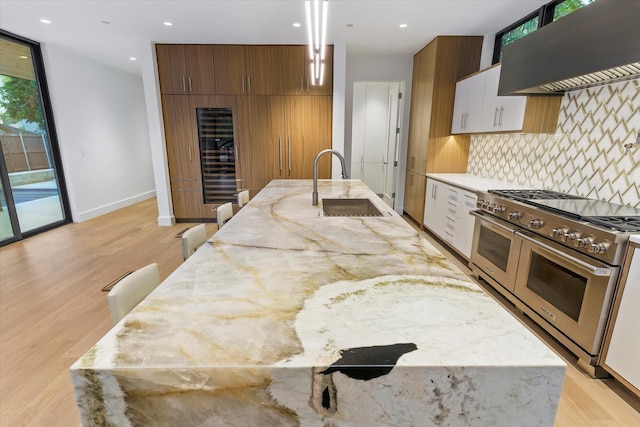 kitchen featuring sink, light hardwood / wood-style flooring, premium range hood, backsplash, and double oven range