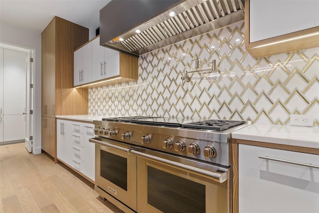 kitchen with light wood-type flooring, premium range hood, tasteful backsplash, range with two ovens, and white cabinetry