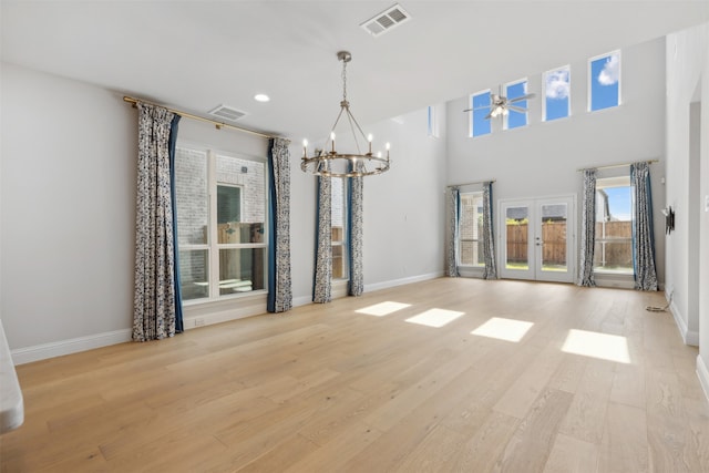 unfurnished dining area with french doors, ceiling fan with notable chandelier, and light wood-type flooring