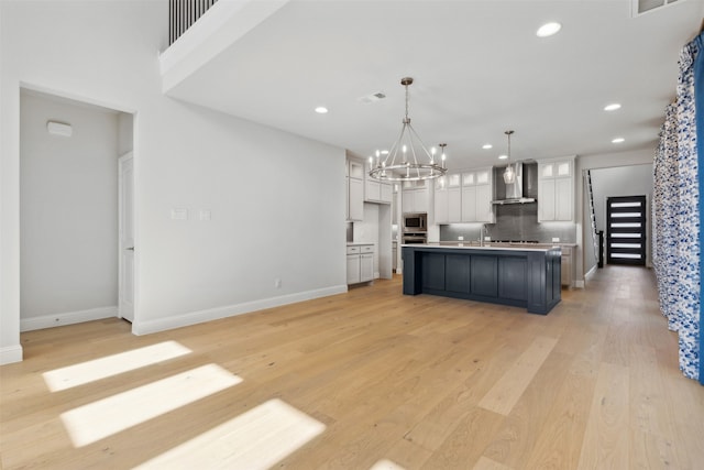 kitchen featuring an island with sink, pendant lighting, light hardwood / wood-style floors, wall chimney exhaust hood, and stainless steel appliances