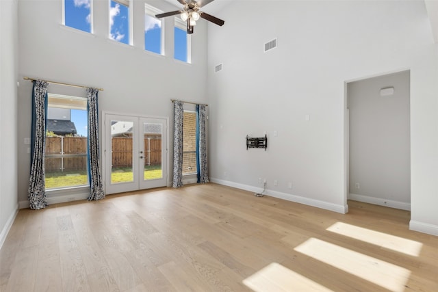 unfurnished living room featuring french doors, light hardwood / wood-style flooring, a towering ceiling, and ceiling fan