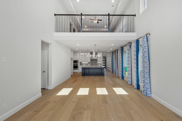 unfurnished living room with light wood-style floors, baseboards, ceiling fan with notable chandelier, and a towering ceiling