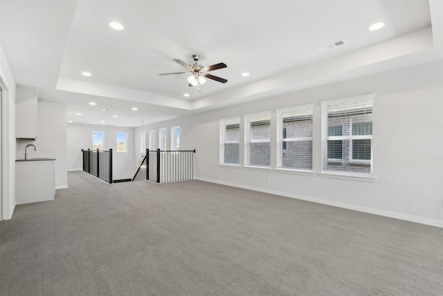 carpeted empty room featuring sink, ceiling fan, a healthy amount of sunlight, and a raised ceiling