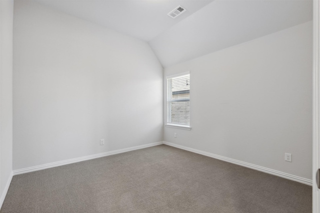 empty room featuring baseboards, vaulted ceiling, dark colored carpet, and visible vents