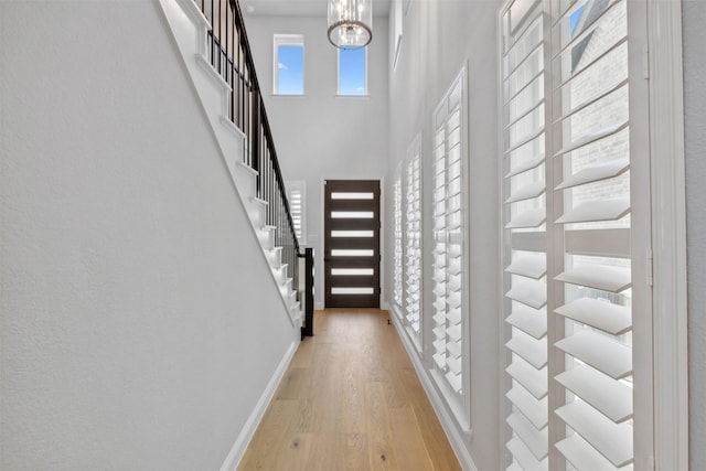 corridor with baseboards, a high ceiling, stairway, and light wood-type flooring