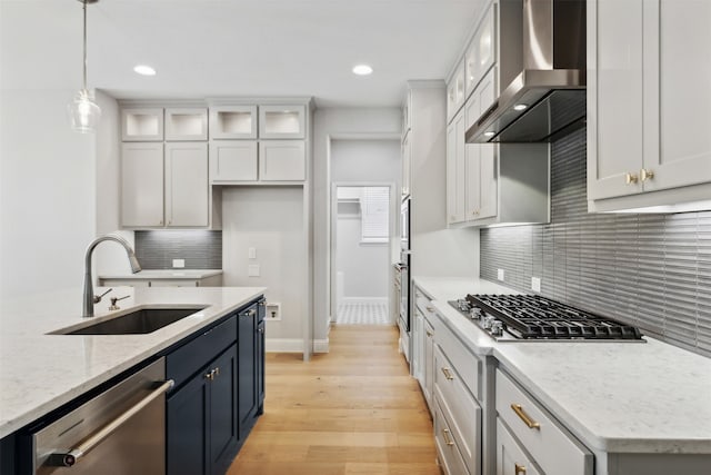 kitchen featuring wall chimney range hood, sink, appliances with stainless steel finishes, light stone counters, and light hardwood / wood-style flooring