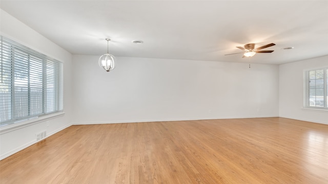 unfurnished room featuring ceiling fan with notable chandelier and light wood-type flooring