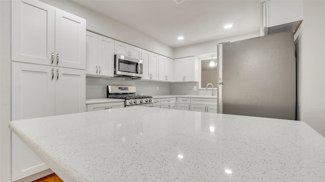 kitchen featuring appliances with stainless steel finishes, sink, white cabinetry, light stone counters, and decorative backsplash