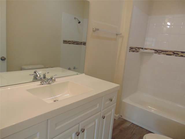 full bathroom featuring tiled shower / bath, vanity, hardwood / wood-style floors, and toilet