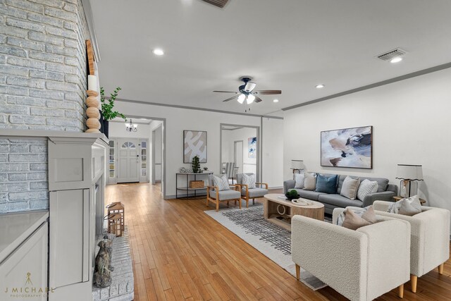 living room featuring ceiling fan, ornamental molding, light hardwood / wood-style flooring, and a fireplace