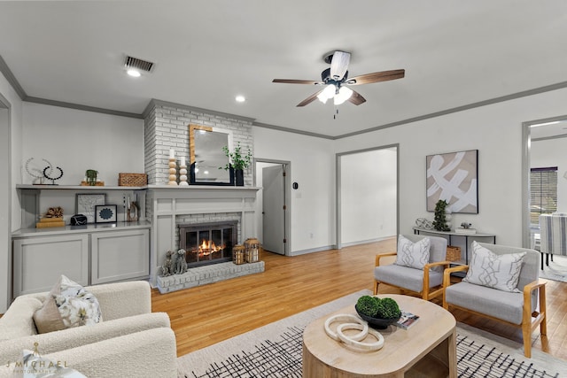 living room featuring light hardwood / wood-style flooring, ceiling fan, crown molding, and a brick fireplace