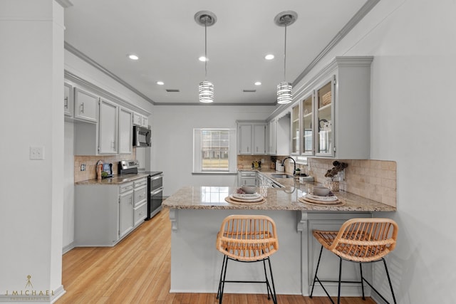 kitchen with kitchen peninsula, a breakfast bar area, light wood-type flooring, pendant lighting, and stainless steel appliances