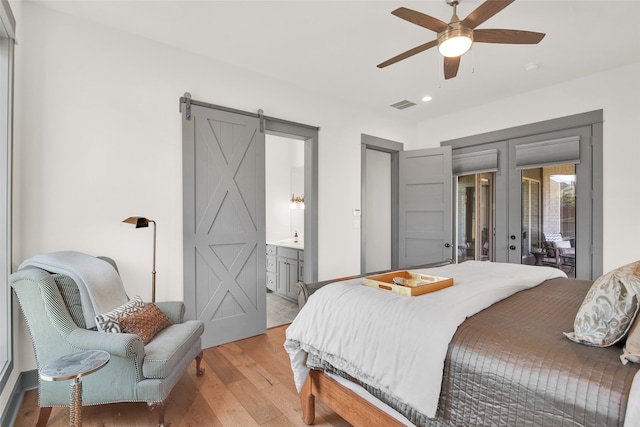 bedroom featuring ceiling fan, access to outside, a barn door, light hardwood / wood-style flooring, and ensuite bath