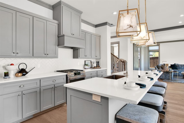 kitchen with high end range, sink, crown molding, gray cabinets, and light hardwood / wood-style floors