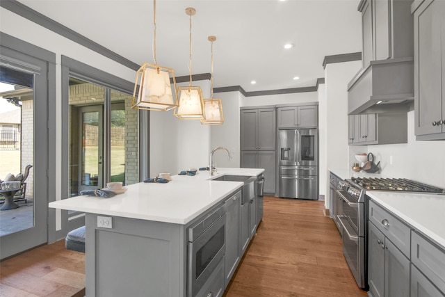 kitchen with hanging light fixtures, an island with sink, hardwood / wood-style flooring, gray cabinetry, and stainless steel appliances